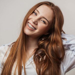 Happy young woman with red hair smiling with braces after a visit at Smile Design Orthodontics Houston TX